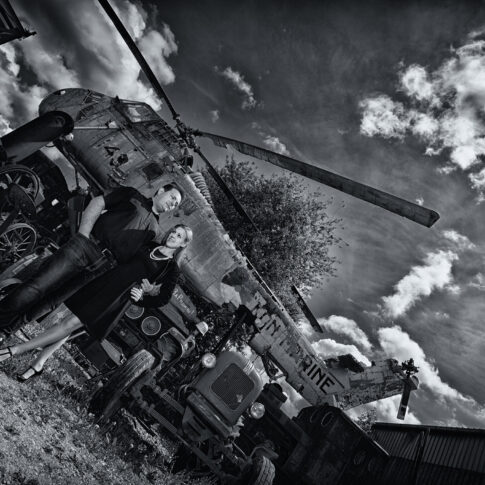 Paar steht Arm in Arm vor einem kaputten Hubschrauber an einem Lost Place